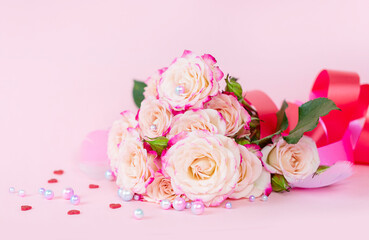 delicate bouquet of bushy peony roses with bright ribbons, pearls, feathers and hearts  on a pink background, the concept of congratulations on Valentine's day
