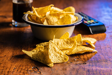 Salted tortilla chips. Yellow nachos triangle and tv remote control
