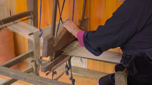 A local woman from black hmong ctribe weaves black fabric on traditional wooden weaving machine in a Cat Cat valley. Sa Pa, Northern Vietnam. Travel to Vietnam concept
