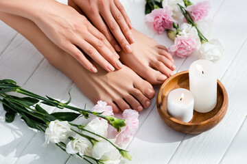Obraz na płótnie Canvas female feet and hands with glossy pink nails near carnation and eustoma flowers and candles on white wooden surface