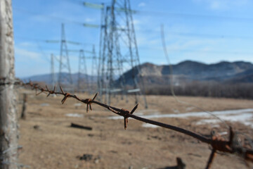 Rusty barbed wire in the foreground, blurred power lines and mountains in the background