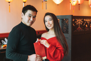 Beautiful young asian couple in red clothes give present in festive chinese vietnamese restaurant...