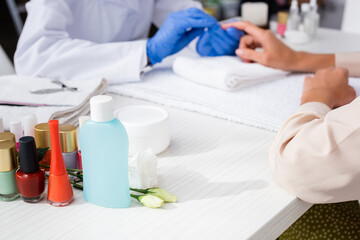 selective focus of bottles with nail varnish and nail polish remover near manicurist and client on blurred background, cropped view
