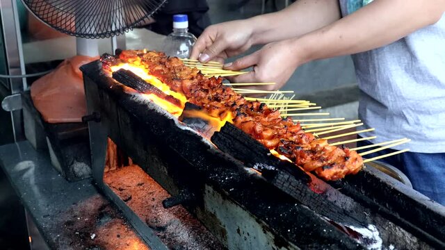 Street hawker preparing to grille beef and chicken satay on traditional charcoal pit