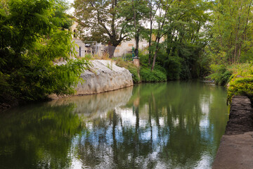 View of the Rosinyol channel of the river Ter where the trees and bushes are reflected in its calm waters. Manlleu, Catalonia, Spain