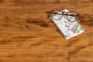 Brown glasses on a white notebook. Wood background.