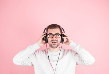 Young man listens to music using headphones. Music technology indoor concept. Isolated casual man on pink background with copyspace