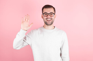 Naklejka premium Friendly positive smiling young caucasian male with stubble and dark hair in a trendy sweatshirt waving hand while greeting friends while having fun indoors. Human relationships and feelings