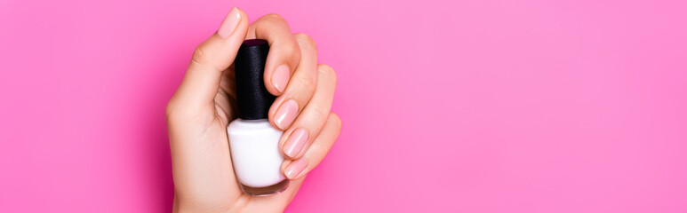 top view of groomed female hand of bottle with white nail polish on pink background, banner