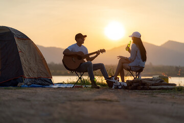 Asian couple with dog playing guitar and drinking beer beside their tent campsite - 404512479