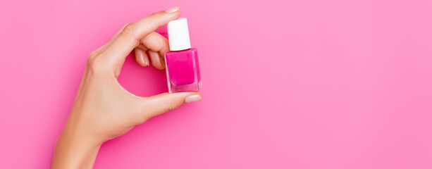 partial view of woman holding bottle of nail enamel on pink background, banner