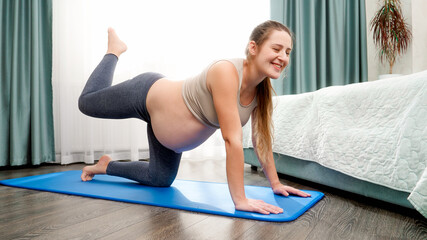 Beautiful smiling pregnant woman with big belly stretching and doing yoga exercise at morning. Concept of healthy lifestyle, healthcare and sports during pregnancy