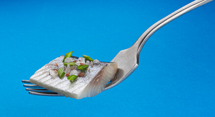 Pieces of salted herring on fork isolated on blue background