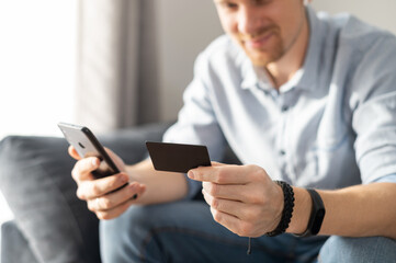 A credit card and smartphone in hands of young intelligent man, online shopping, e-banking. Focus on credit card