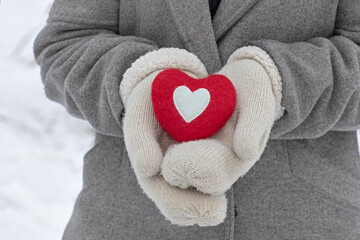 red woolen heart in female hands, white knitted gloves, background for valentine's day, i love winter