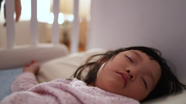 Asian mother tuck in blanket her cute kid on the bed. Concept for mom goodnight daughter. 4K Video slow motion.