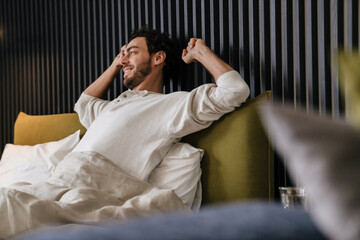 Joyful man listening music using mobile phone while lying in bed