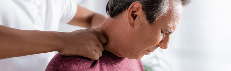 Fototapeta premium african american physiotherapist massaging middle aged man in clinic, banner