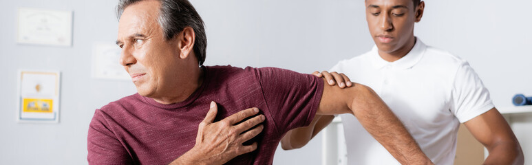 african american physiotherapist working with mature man in clinic, banner