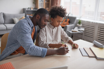 Portrait of caring African-American father helping son doing homework or studying while sitting...