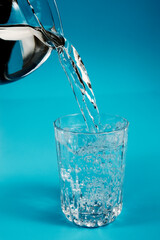 Pouring drinking clean water from a pot into a glass on a blue background