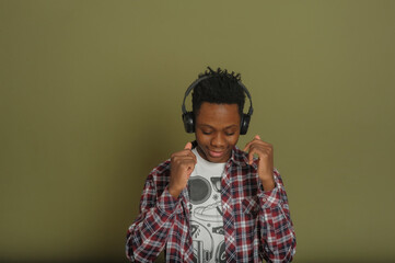 Fototapeta premium young african american man listening to music with headphones, smiling and dancing on green background