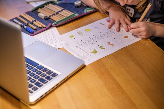 Schulkind mit Computer und Arbeitsbl&auml;ttern am Tisch beim Homeschooling im Distanzunterricht