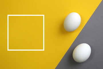 Two chicken white eggs lie on yellow and gray colors, next to there is a frame for text