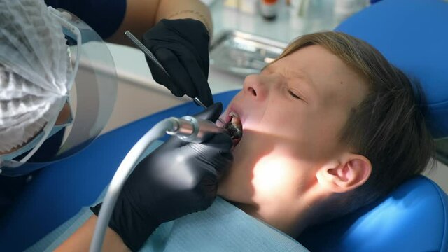 Dentist hygienist making oral hygienic cleaning in dentistry for teen child boy, face closeup. Using professional electrical equipment dental drill machine to brush teeth in dentistry, visit doctor.