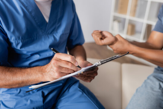 partial view of doctor writing prescription near injured african american man on blurred background