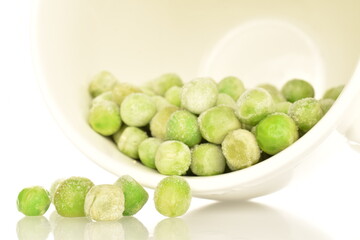 Organic frozen green peas in a white ceramic cup, close-up, isolated on white.