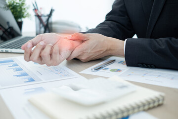 Obraz premium Businessman grasping the painful wrist caused by prolonged work on a laptop keyboard. Wrist numbness Arthritis While working at the office