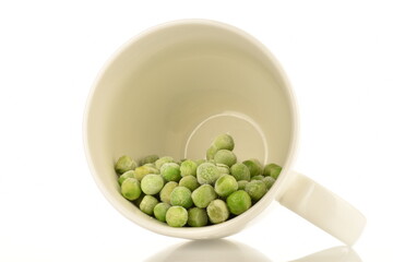 Organic frozen green peas in a white ceramic cup, close-up, isolated on white.