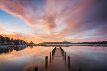 Peaceful colourful jetty sunrise with reflections by Windermere in the Lake District