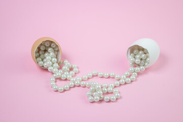 White beads scattered from the broken egg. Beads on a pink background. Women's bijouterie. Everyday decoration.