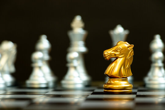 Gold knight in chess game face with the another silver team on black background (Concept for company strategy, business victory or decision)