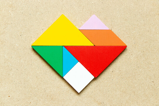 Color tangram puzzle in heart shape on wood background