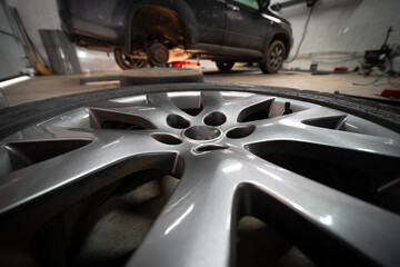 In the foreground is a wheel on the floor. In the background is a car. Service and maintenance concept. Planned and sudden. Replacement of brake pads. Selective focus