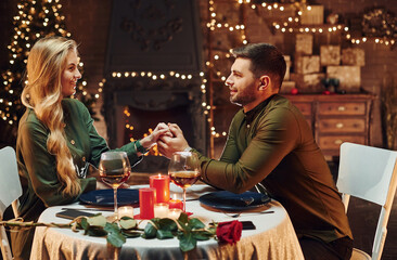 Holding by the hands. Young lovely couple have romantic dinner indoors together