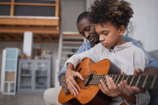 Mature man spending spare time with his son at home, teaching him how to play beautiful song on guitar