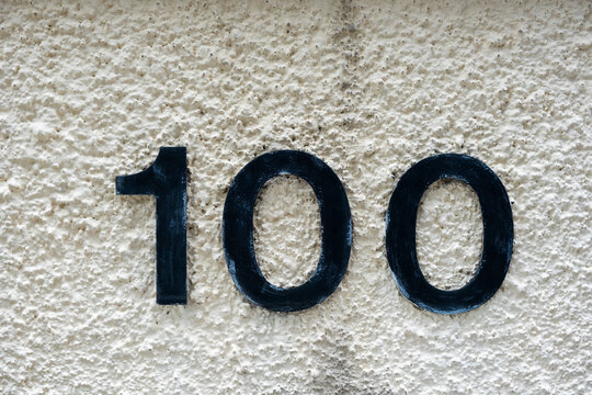 House number 100 on a white weathered textured wall. Stock Photo.