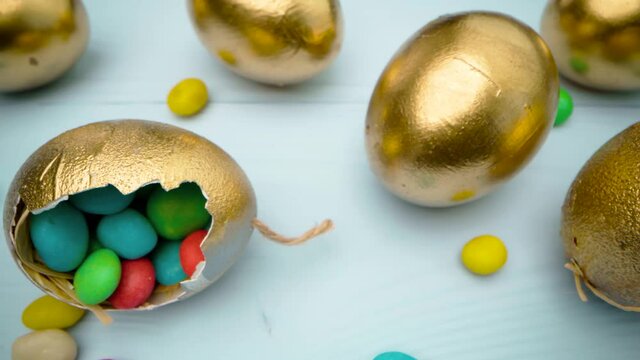 Golden decorative Easter eggs filled with colorful candies on wooden table close up