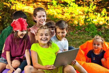 Children play in nature with a laptop. Boys and girls are resting in a tent camp. Children sit on the carpet on the grass in summer.