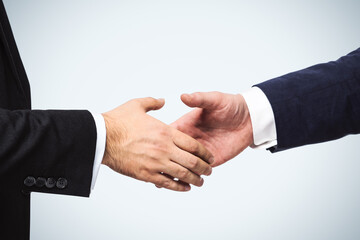Two businessmen shake hands on a white wall background, deal concept, close up