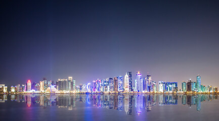 Fototapeta premium (Selective focus) Stunning panoramic view of the Doha Skyline illuminated at dusk during the Covid-19 pandemic. Doha is the capital and most populous city of the State of Qatar.