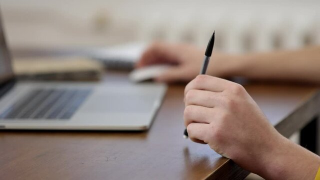 Close up of male hands working at a laptop. In one hand, the guy turns a pen. The concept of working with information.