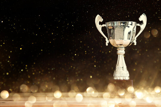 image of silver trophy over wooden table and dark background, with abstract shiny lights