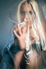 Trapped woman. Defocused art portrait. Lockdown isolation. Keep distance. Helpless lady touching looking through transparent plastic film isolated on gray blur.