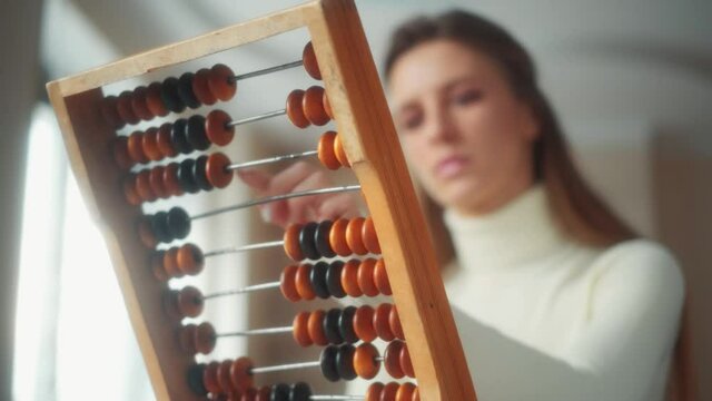 A female is calculating with balls on wooden abacus for number calculation. The concept of finance management and savings