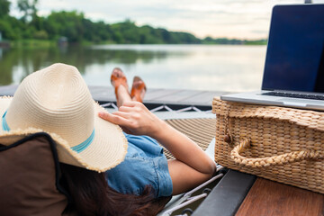 Work and Vacation Concept - Trendy hipster girl relaxing and lying in a hammock working at a laptop at sunset or sunrise. Selective focus